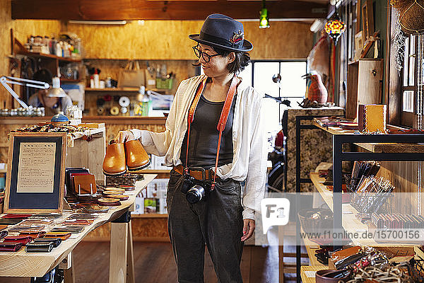 Japanische Frau mit Hut und Brille beim Stöbern in einem Ledergeschäft.