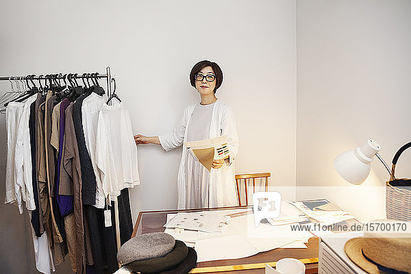 Japanese woman wearing glasses working at a desk in a small fashion boutique.