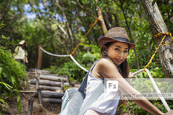 Japanese woman wearing hat hiking in a forest.
