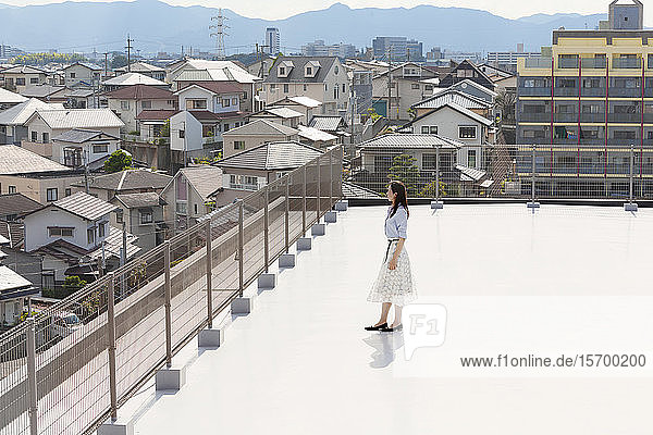 Hochwinkelaufnahme einer Japanerin  die auf einem Dach in einer städtischen Umgebung steht.
