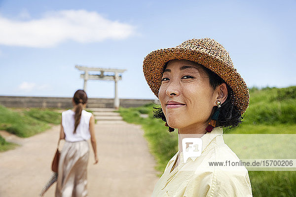 Zwei Japanerinnen mit Hüten stehen auf einem Weg  im Hintergrund der Shinto-Schrein.