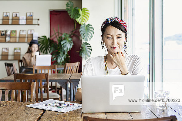 Japanische Fachfrau  die an einem Tisch in einem Arbeitsraum sitzt und einen Laptop benutzt.
