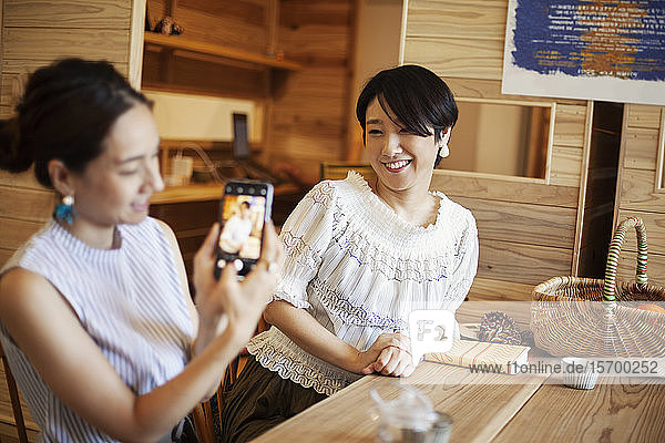 Two Japanese women sitting at a table in a vegetarian cafe  using mobile phone.