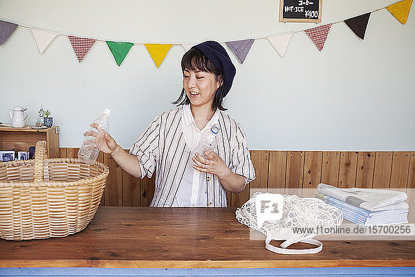 Japanerin  die in einem Hofladen steht und durchsichtige Plastikflaschen in einen Korb sortiert.