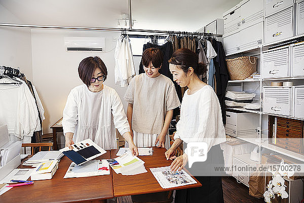 Drei Japanerinnen stehen an einem Tisch in einer kleinen Modeboutique und schauen sich Stoffmuster an.