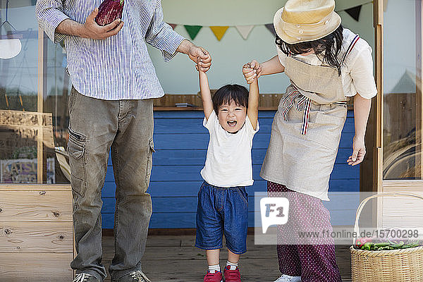 Japanischer Mann  Frau und Junge stehen vor einem Bauernladen und halten Händchen.