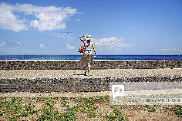 Japanese woman wearing hat standing on a wall  ocean in the background.