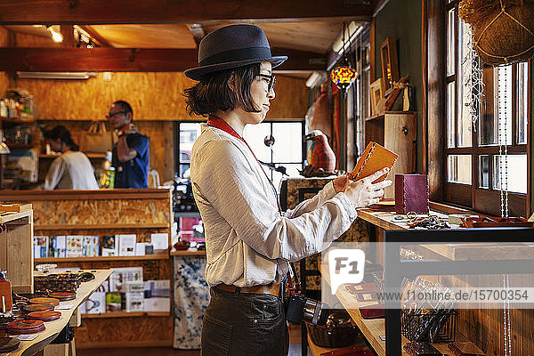 Japanese woman wearing hat and glasses browsing merchandise in a leather shop.