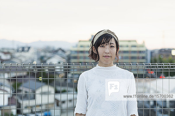 Japanerin  die auf einem Dach in einer städtischen Umgebung steht und in die Kamera schaut.