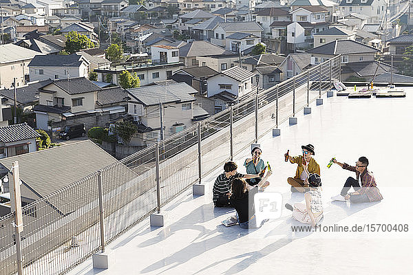Hochwinkelansicht einer Gruppe junger japanischer Männer und Frauen  die auf einem Dach in einer städtischen Umgebung sitzen.