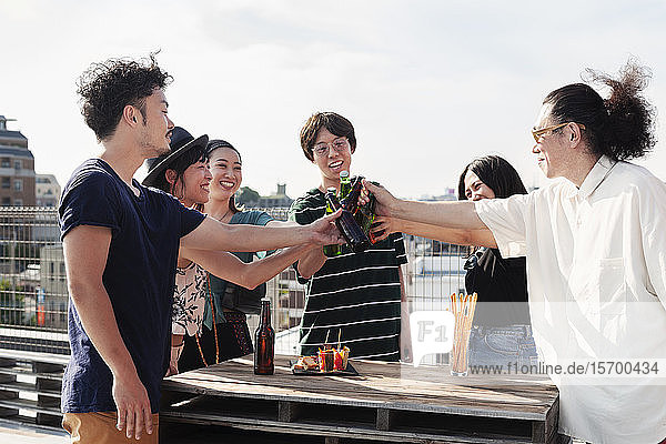 Gruppe junger japanischer Männer und Frauen  die auf einem Dach in einer städtischen Umgebung stehen und Bier trinken.