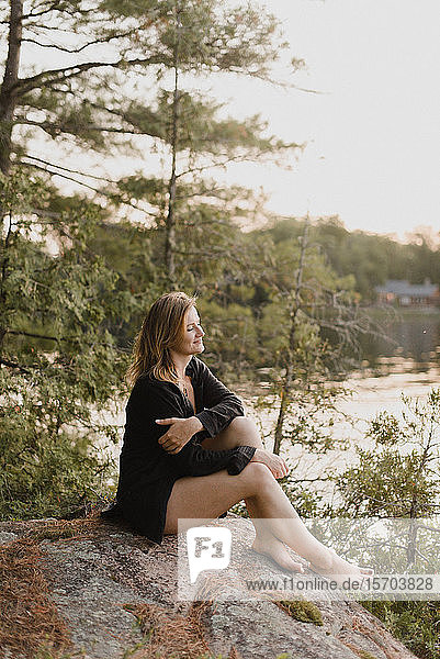 Woman relaxing on boulder by lake Bobcaygeon Ontario Canada