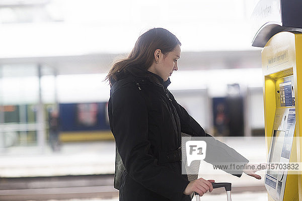 Young woman at ticket machine in train terminal
