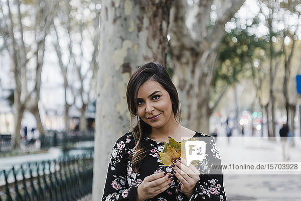 Porträt lächelnde junge Frau hält Herbstblätter im Stadtpark
