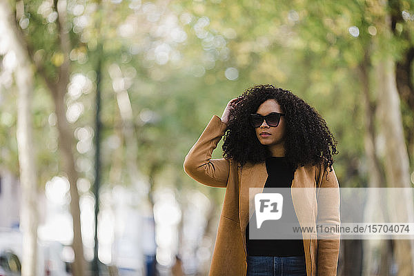 Stylish young woman in sunglasses walking in park