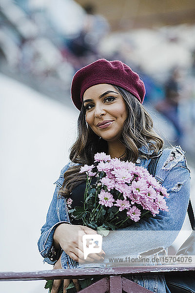 Porträt einer lächelnden jungen Frau mit Baskenmütze  die einen Blumenstrauß hält
