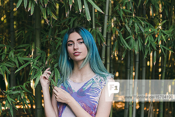 Porträt junge Frau mit blauem Haar unter Bambusbäumen stehend