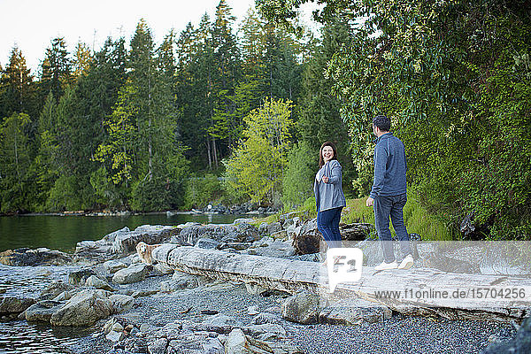 Glückliches Paar beim Spaziergang auf einem umgestürzten Baumstamm am Seeufer im Wald  Mill Bay  British Columbia  Kanada