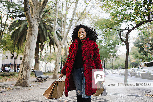 Portrait carefree young woman with shopping bags on urban sidewalk