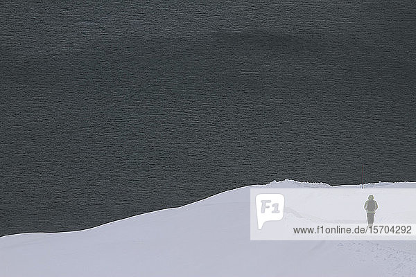 Schneeschuhwanderer am verschneiten Hang mit Blick auf den See