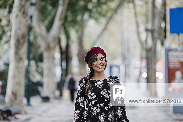 Porträt lächelnde junge Frau mit Baskenmütze auf städtischem Bürgersteig