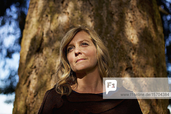 Porträt heitere Frau stehend am sonnigen Baumstamm