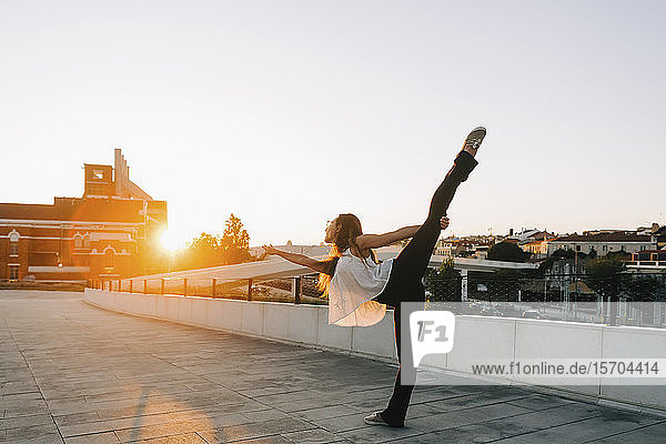 Anmutige junge Tänzerin im stehenden Spagat in einem sonnigen Stadtpark