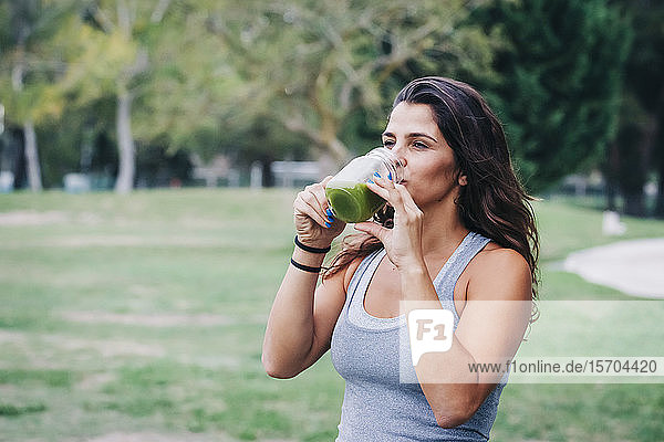 Fit female personal trainer drinking green smoothie in park