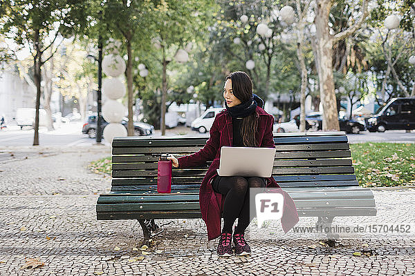 Frau mit Wasserflasche arbeitet am Laptop im herbstlichen Stadtpark
