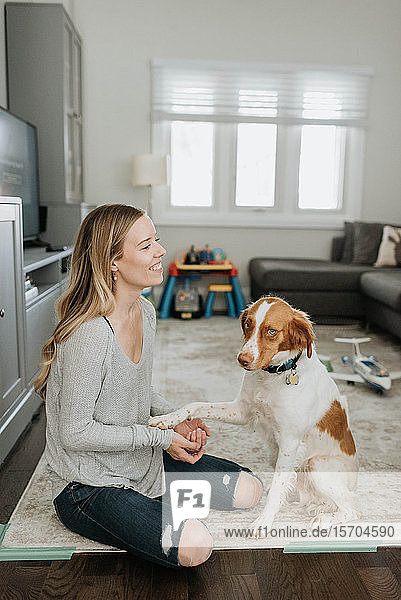 Frau hält Pfote eines Haushundes im Wohnzimmer