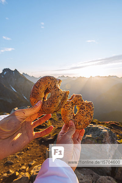 Hands holding bagel against sun  Winchester Mountain  North Cascades  Washington  USA