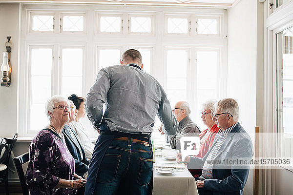 Besitzerin steht am Tisch älterer Freunde im Restaurant