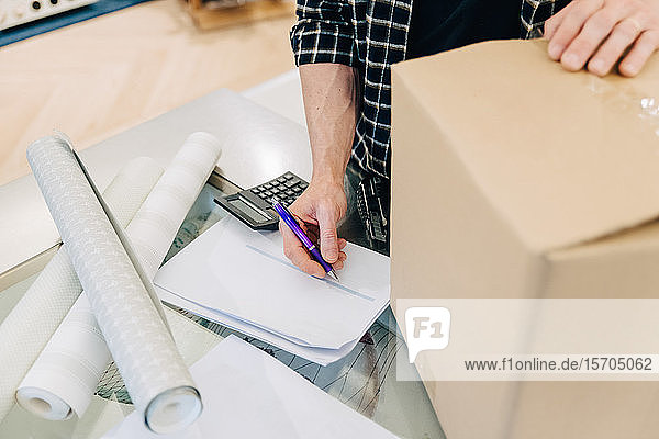 Midsection of salesman checking document by cardboard box in store