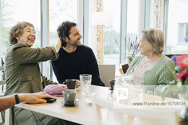 Smiling man sitting amidst senior women at dining table in retirement home