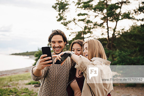 Fröhliche Freunde  die sich am Strand am Smartphone vergnügen