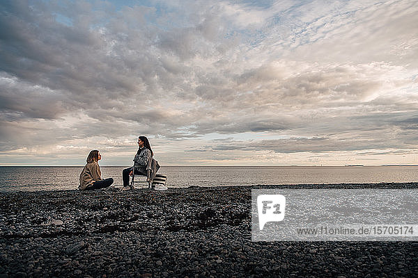 Freunde unterhalten sich  während sie sich am Meeresufer am Strand vor bewölktem Himmel ausruhen