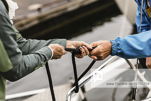 Abgehackte Hände einer Ausbilderin und eines älteren Mannes  die ein Seil an der Reling einer Yacht binden