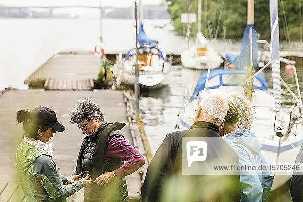 Weibliche Ausbilderin hilft älteren Männern und Frauen beim Bootsführerkurs über Schwimmwesten