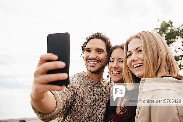 Smiling man taking selfie with friends on smart phone against sky
