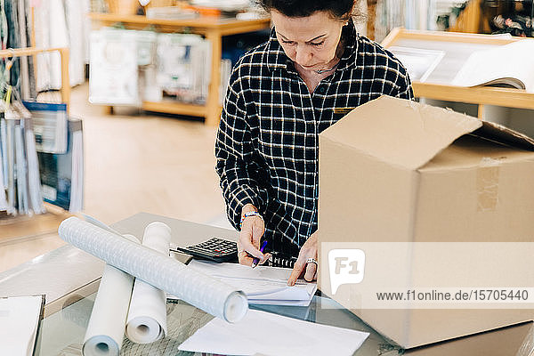 Saleswoman reading document with box on table in store