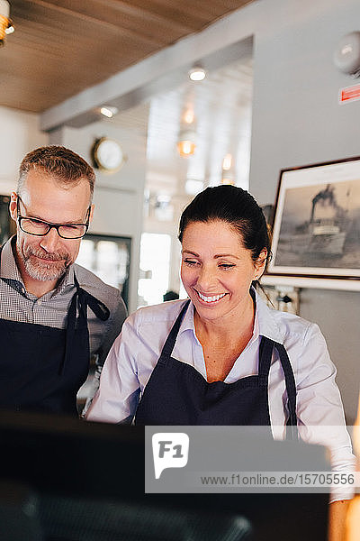 Smiling owners using computer in restaurant