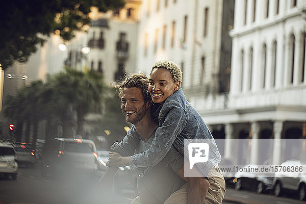 Happy young man carrying girlfriend piggyback in the city