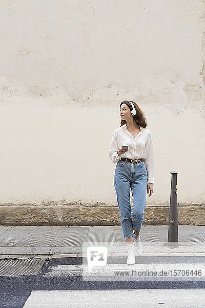 Young woman with smartphone and headphones crossing the street