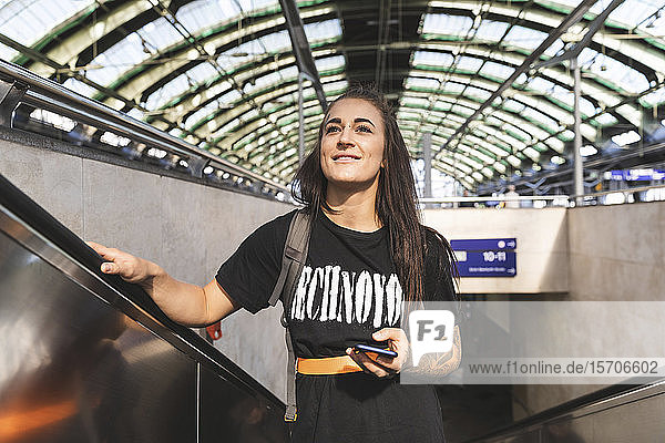 Porträt einer lächelnden jungen Frau  die auf einer Rolltreppe am Bahnhof steht  Berlin  Deutschland