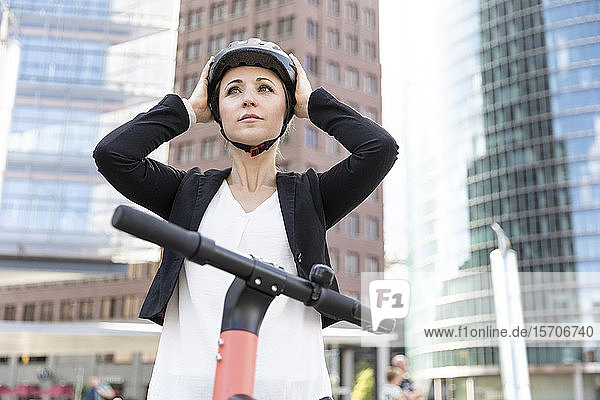 Frau mit E-Scooter in der Stadt  die einen Helm aufsetzt  Berlin  Deutschland