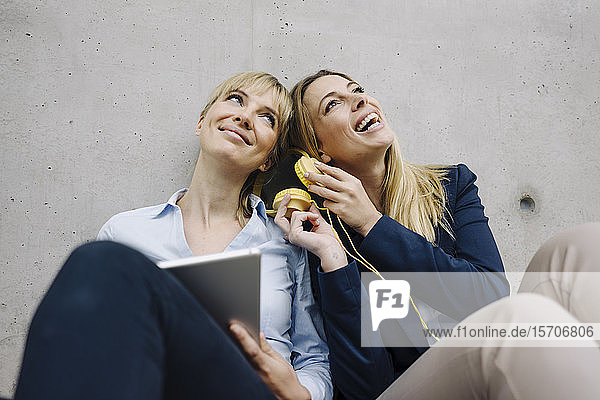 Two happy young businesswomen sharing headphones