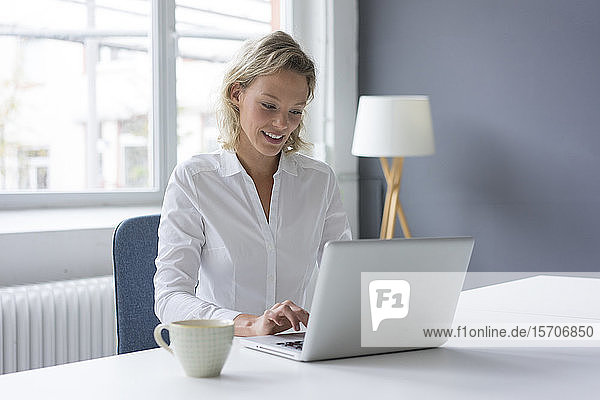 Lächelnde junge Geschäftsfrau mit Laptop am Schreibtisch im Büro