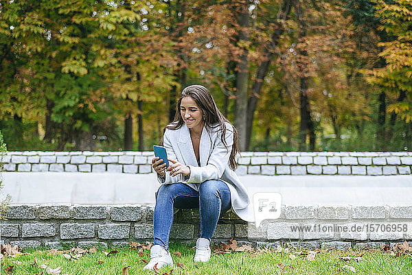 Lächelnde Frau benutzt ihr Smartphone in einem Park