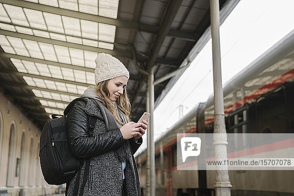 Smiling young woman with backpack standing on platform looking at cell phone  Vilnius  Lithuania