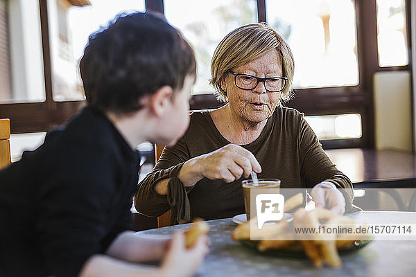 Grandmother and grandson having breakfast at table at home together